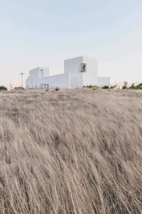 A minimalist white house surrounded by dry grass in a canyon landscape.