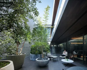 A modern outdoor lounge area with concrete planters, chairs, and a table.