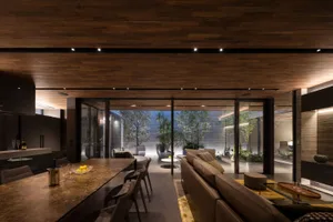 A modern living room with wooden elements, including a brown leather sofa, a glass dining table, and a wooden ceiling with re