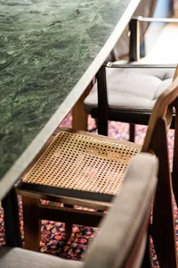 A modern restaurant interior featuring a concrete countertop and wooden chairs with woven seats.