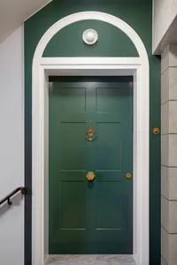 A green door with a brass knocker and handles, framed by white trim and a dark green ceiling.