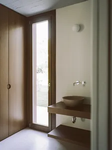 A minimalist bathroom with wooden elements, featuring a small sink and a large window.