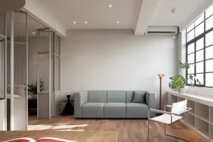 Modern minimalist living room featuring a grey fabric sofa, white chair, and potted plant.
