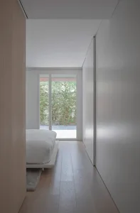 Contemporary bedroom featuring a white bed with minimalist wooden flooring, large windows offering natural light.
