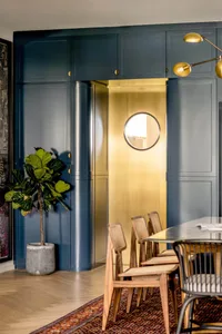 A modern dining room with blue cabinets and a brass door with a circular window.