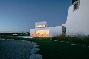 A modern house with white painted exterior and concrete terraces viewed at night with lights on showing interior space.