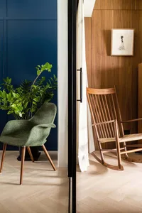A modern interior living room with a wooden rocking chair and green armchair.