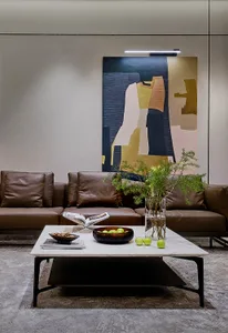 A modern living room with a leather sofa, marble coffee table, and glass vase with greenery on a grey carpet.