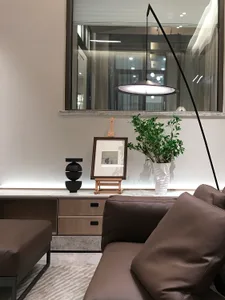A modern living room featuring a brown leather sofa, a hanging lamp, and a plant on a wooden shelf.