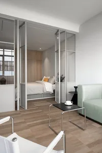 Modern minimalist bedroom with a glass-enclosed sleeping area, wooden flooring, and mint green sofa.