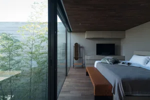 Modern minimalist bedroom with glass walls and wooden floor.