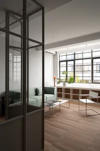 A modern minimalist living room featuring a wooden floor, white walls, a green sofa, and a potted plant.