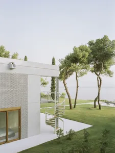 A minimalist residential exterior with a spiral staircase, white exterior walls, and greenery.