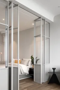 A minimalist bedroom featuring a glass partition, white bedding, and a small black table with a black vase.