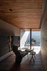 A minimalist living room with a wooden floor, walls, and ceiling, featuring a comfortable armchair and a side table.