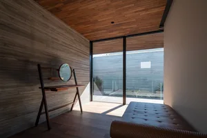 A minimalist living room with wooden walls and flooring, featuring a wooden console table with a circular mirror.