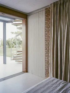 Minimalist bedroom featuring white curtains, wood paneling, and concrete elements.