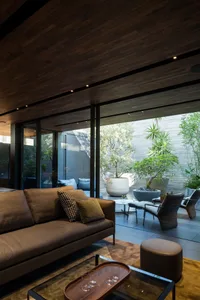 A minimalist living room featuring wood-paneled walls, a glass coffee table, and a brown leather sofa.