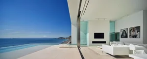 Modern minimalist living room featuring glass and concrete walls with a stunning sea view.