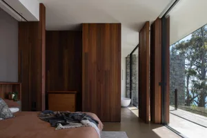 Modern bedroom featuring wooden walls and floor-to-ceiling glass windows with a view of nature.