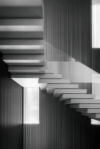 A modern staircase made of concrete with a glass railing against a wall of vertical lines.
