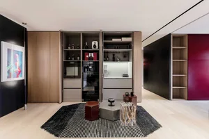 A modern kitchen featuring brown wood cabinets, shelves with bottles, and a coffee machine, illuminated by overhead lighting.
