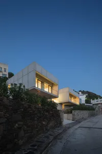 現代住宅混凝土外觀在黃昏時分被燈光照亮，位於街道上。