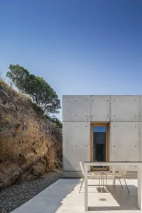 A modern, minimalist residential exterior with a concrete wall and a single glass door.