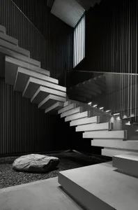 A modern staircase made of graphite concrete with a glass railing and a large rock in the foreground.