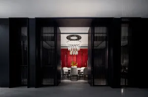 Modern dining room featuring a black glass table, black metal bar, red laminate backdrop, and opulent chandelier hanging from