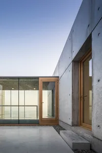 Modern house exterior featuring concrete walls and large glass windows.