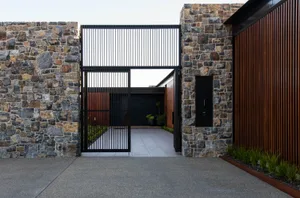 A modern house with stone and concrete exterior features a large gate and a wooden slatted wall.