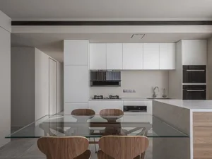 Modern kitchen with white cabinets, concrete countertops, wooden furniture, and a glass table top.