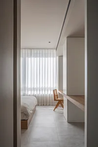 A modern minimalist bedroom featuring a white bed, light-grey flooring, and wood furniture.