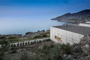 一座以混凝土建造的現代住宅建築，坐落於海濱，可眺望海洋與山景