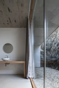 A minimalist bathroom with concrete walls and floor, featuring a wooden vanity with a circular mirror and a white vessel sink