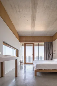 A modern bedroom featuring a clean, minimalist design with concrete flooring and wood accents.