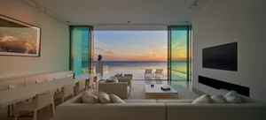 Modern living room featuring large glass doors overlooking the ocean at sunset.