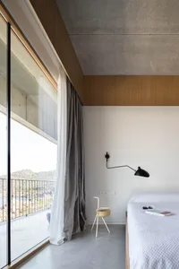 Modern minimalist bedroom featuring concrete walls, glass windows, and metal accents.