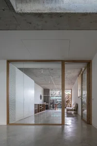 A minimalist bedroom with concrete walls and floor, featuring modern furniture and a large window.