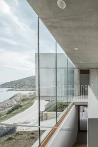 Modern residential interior featuring glass and concrete materials, overlooking a coastal landscape.