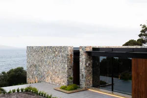 A modern residential exterior with stone walls and glass windows overlooking the ocean.