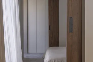 Minimalist bedroom with white walls, a wooden cupboard, and a bed covered in white bedding.