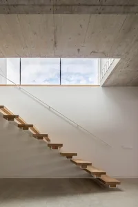 Modern staircase with wooden treads and concrete structure under a large window.