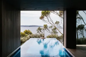 Person in a modern house with a glass infinity pool overlooking a teal-colored skyline.