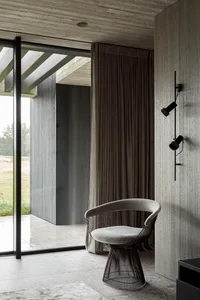 A minimalist interior space featuring a concrete wall, a chair with a wireframe base, and a window with a curtain.