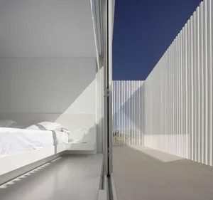 A minimalist bedroom with a white bed and a concrete wall
