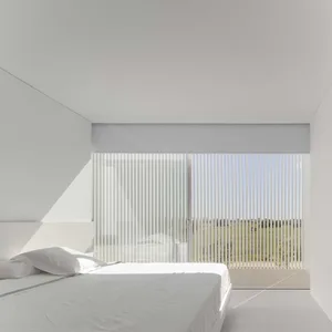A minimalist bedroom with a white bed and wooden blinds.