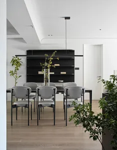 A modern dining room with a minimalist design, featuring a black table, white chairs, and a black shelving unit with books.