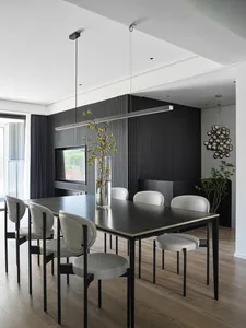 A modern dining room featuring a black metallic pendant light, white leather chairs, and a wooden dining table.